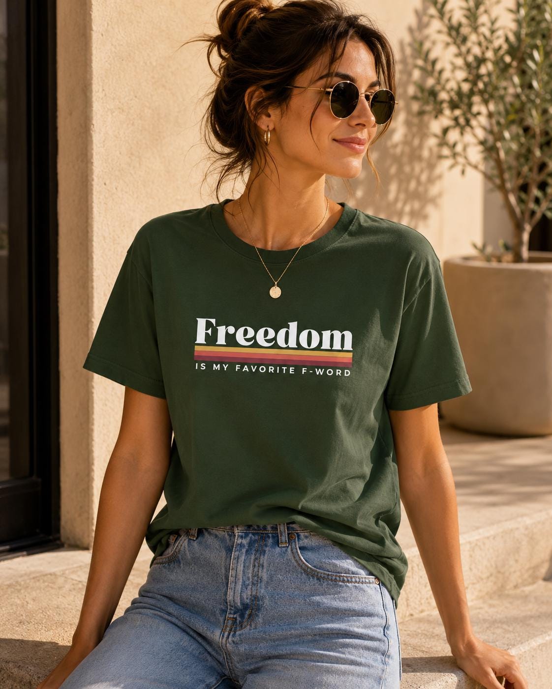 May include: A dark olive green short-sleeve t-shirt featuring the white text Freedom followed by a horizontal striped graphic in yellow, orange, and red, with the additional white text IS MY FAVORITE F-WORD printed underneath.